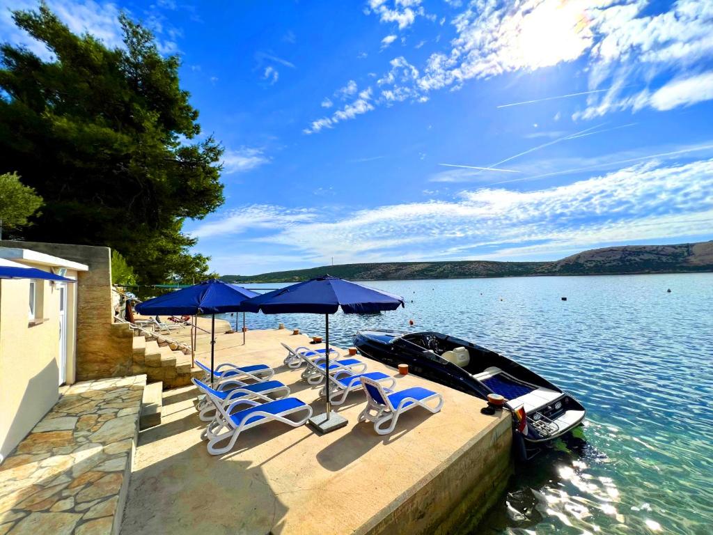 a dock with chairs and umbrellas and a boat on the water at Villa Olivija-direkt am Strand! in Stara Novalja