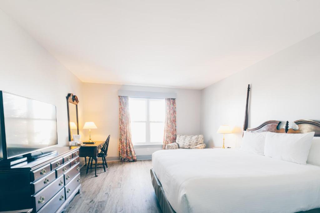 Un dormitorio con una cama, un escritorio y un televisor. en The Loyalist Country Inn & Conference Centre, en Summerside
