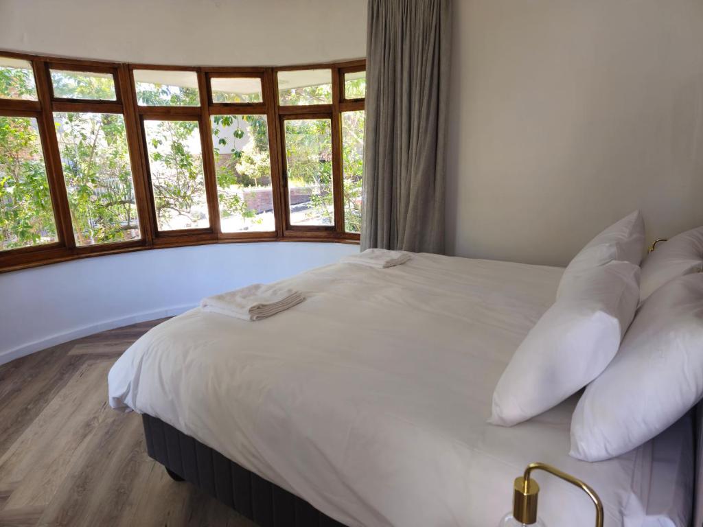 ein weißes Bett mit Kissen in einem Zimmer mit Fenstern in der Unterkunft WunderLux in Kapstadt