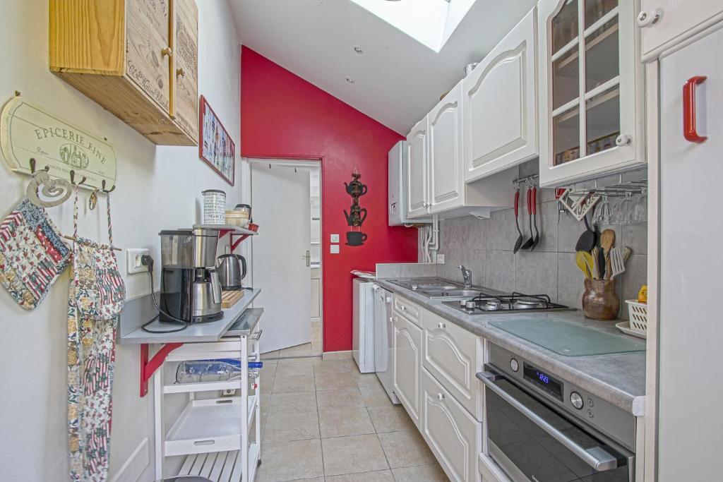 una cocina con armarios blancos y una pared roja en La Maison du Pêcheur, en Étretat