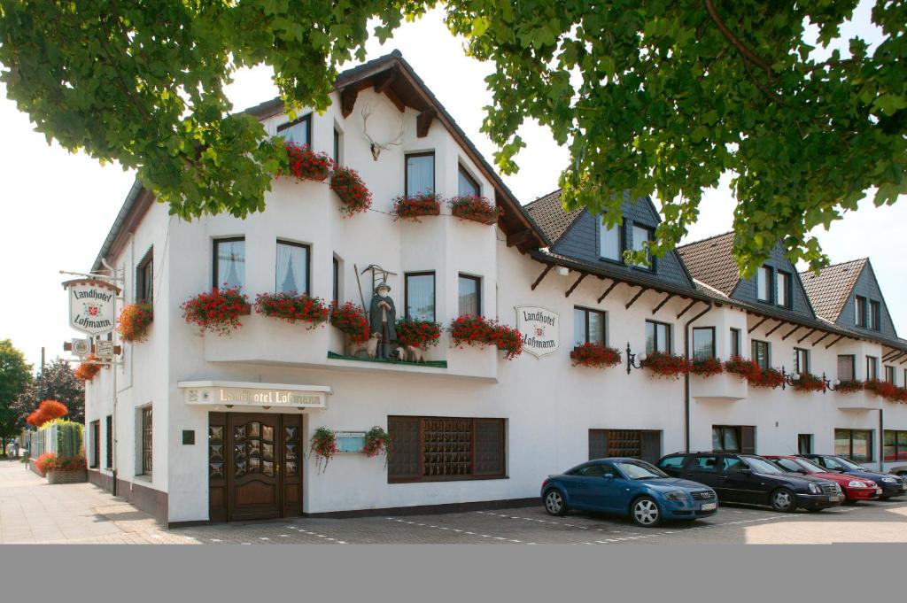 un bâtiment blanc avec des voitures garées devant lui dans l'établissement Landhotel Lohmann, à Langenfeld