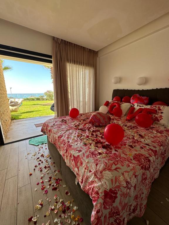 Un dormitorio con una cama con almohadas rojas y una gran ventana. en OCEAN VIEW, Prestigia Plage des Nations en Sidi Bouqnadel