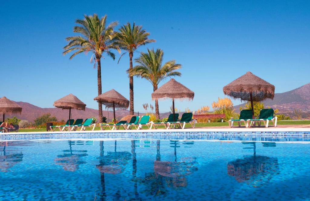 a swimming pool with chairs and umbrellas and palm trees at Beautiful luxurious 2 bedroom apartment with a breathtaking view at La Cala Golf in La Cala de Mijas