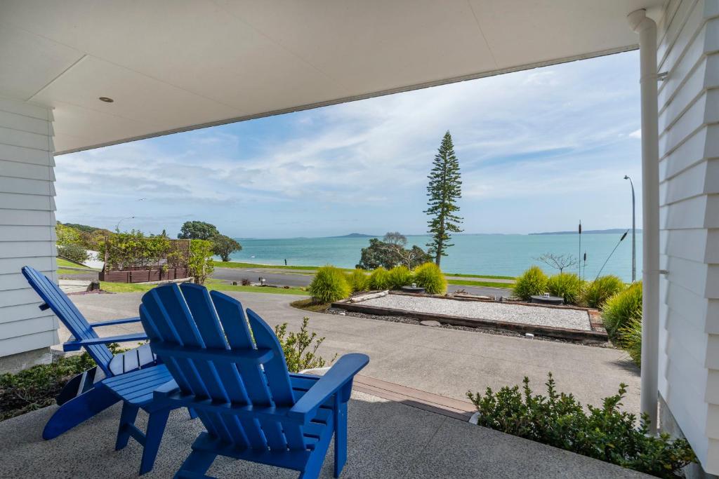 - deux chaises bleues assises sur une terrasse couverte donnant sur l'océan dans l'établissement Maraetai Couples Retreat - Omana Beach Apartment, à Auckland