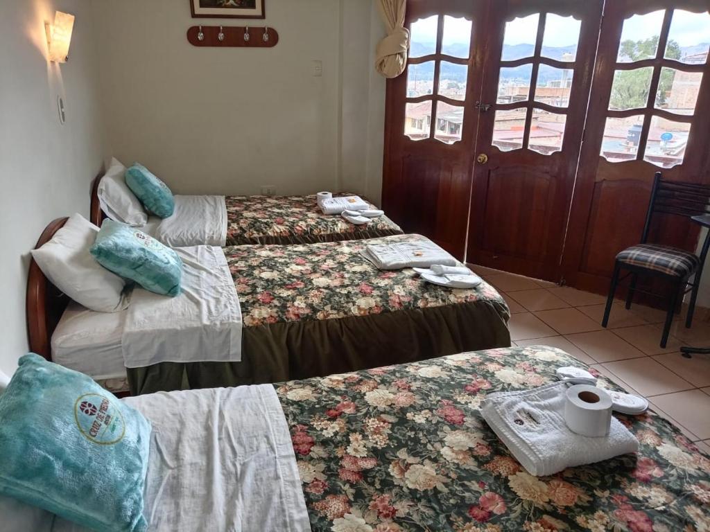 a hotel room with three beds and a table at Hostal Turismo Cruz de Piedra EIRL-Cajamarca in Cajamarca