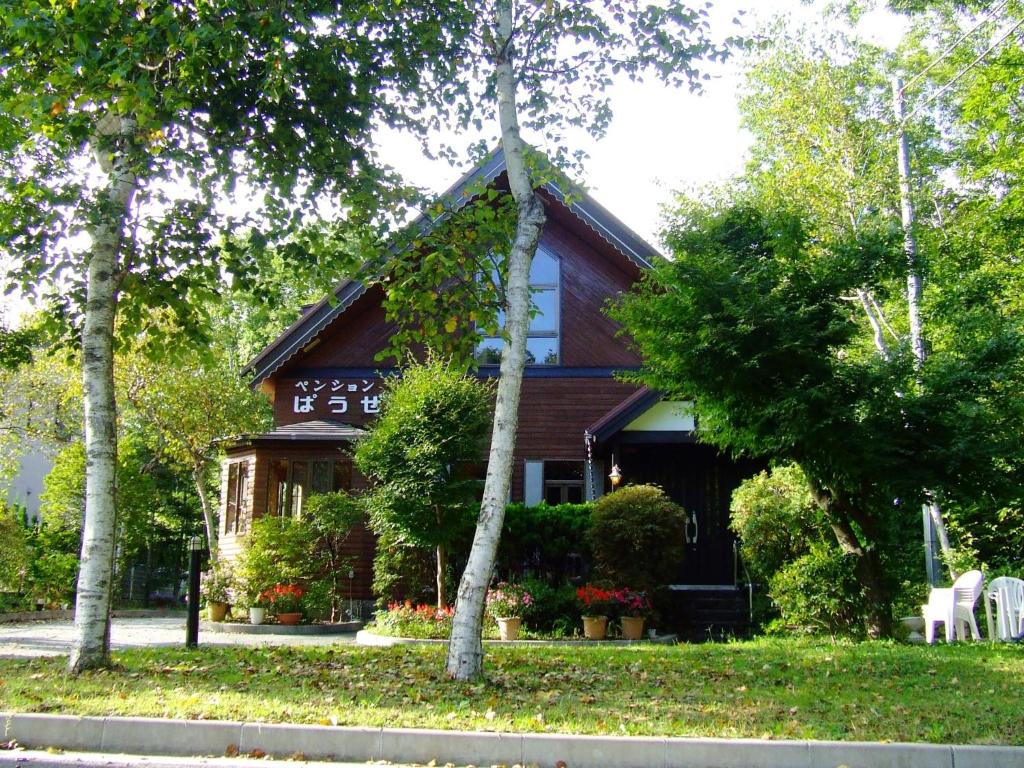 una casa con techo de gambrel con sillas blancas y árboles en Minamitsuru-gun - Hotel / Vacation STAY 45545 en Yamanakako