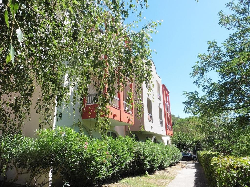 um edifício vermelho e branco com árvores e arbustos em Studio Lamalou-les-Bains, 1 pièce, 2 personnes - FR-1-451-76 em Lamalou-les-Bains