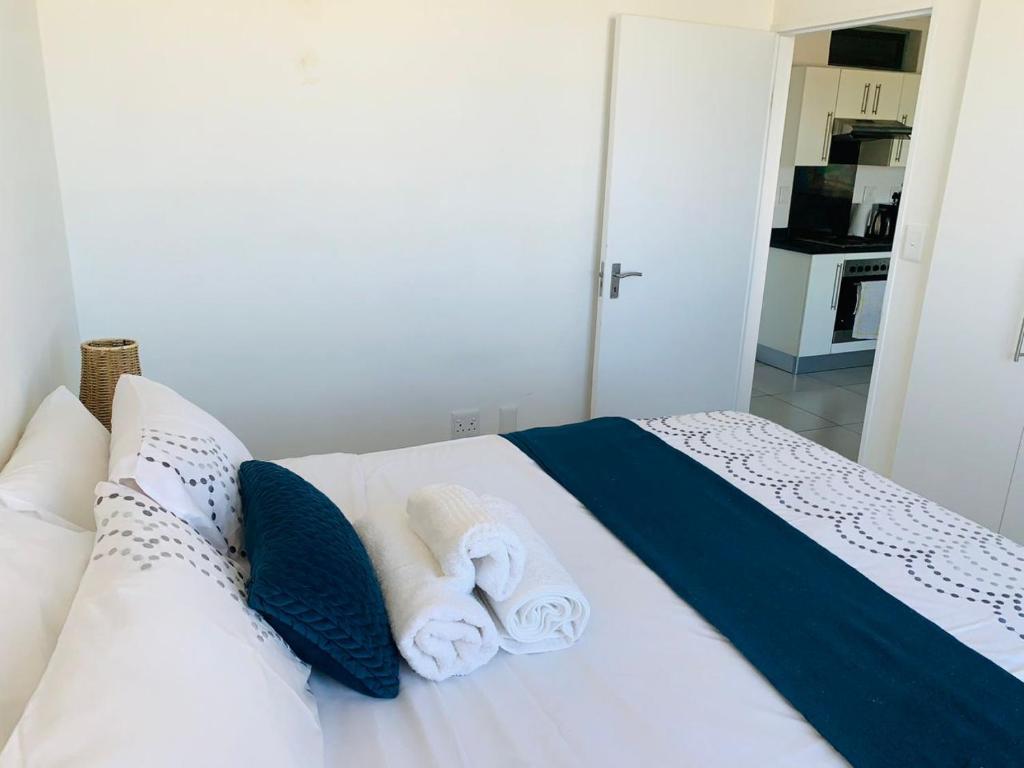 Una cama blanca con almohadas azules y toallas. en Dmn City Apartment at Junction en Windhoek