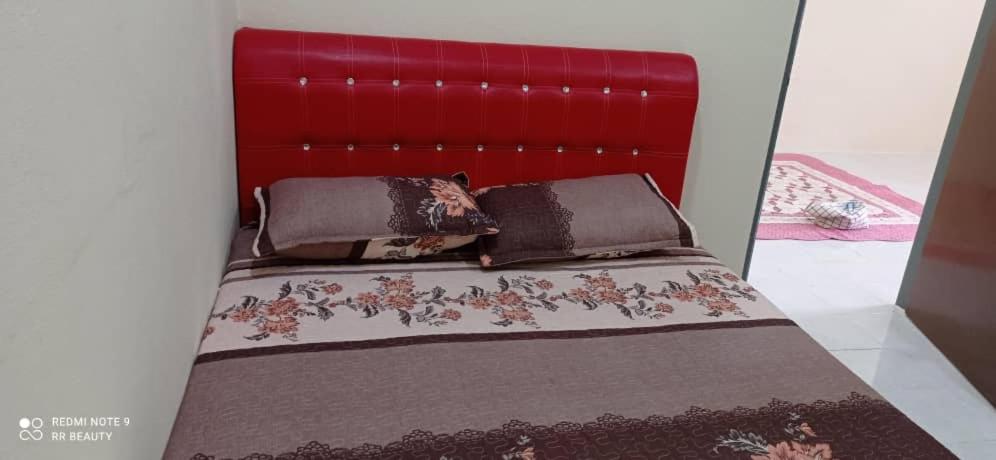a bed with a red headboard in a room at Homestay CikguRose UMK in Bachok