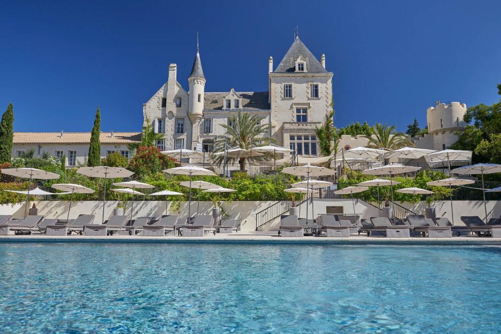 a pool with chairs and umbrellas in front of a building at Château Les Carrasses in Capestang
