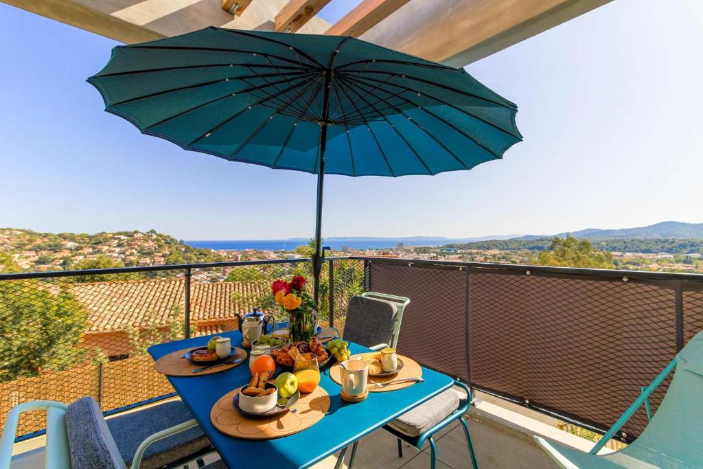 a blue table with an umbrella on a balcony at SELECT'soHOME - Appartement face à la mer avec piscine à Bormes-les-mimosas - CAPNAT-C04 in Bormes-les-Mimosas