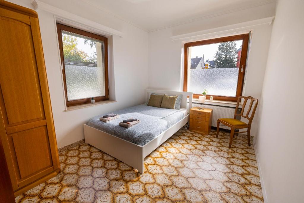 a bedroom with a bed and a chair and two windows at Good connection Airport & City in Luxembourg