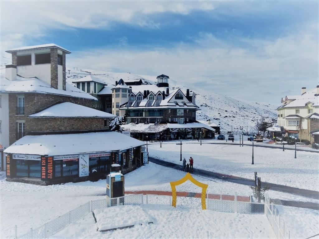 eine schneebedeckte Stadt mit einem Gebäude im Hintergrund in der Unterkunft SKI & SNOW APARTMENTOS by TODOSIERRANEVADA - Plaza Principal Junto a los Telecabinas in Sierra Nevada