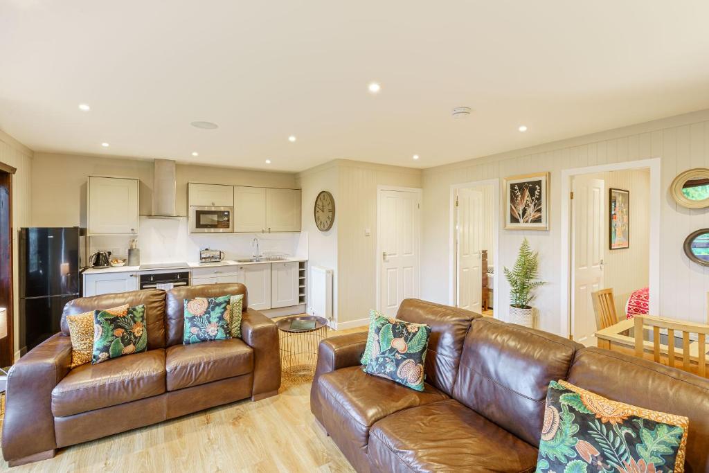 a living room with two leather couches and a kitchen at Conifer Lodge 25 with Hot Tub in Newton Stewart