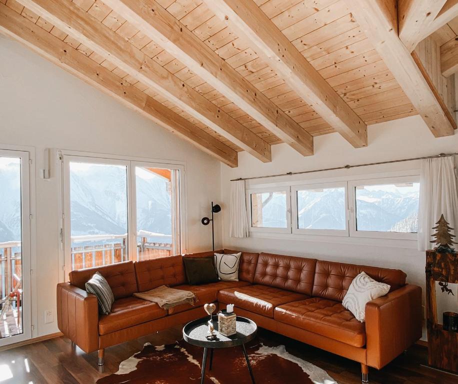 a living room with a brown leather couch and windows at Bergquelle Dachwohnung in Bettmeralp