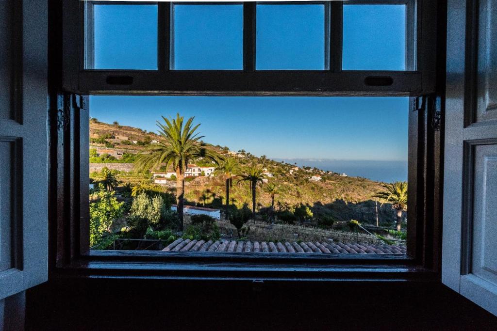 a window with a view of a mountain and palm trees at Casa Tajonaje - Entorno rural in Alajeró