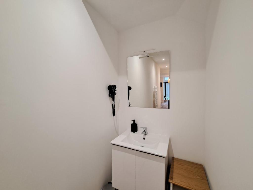 a white bathroom with a sink and a mirror at Maputo - Appartement climatisé in Reims