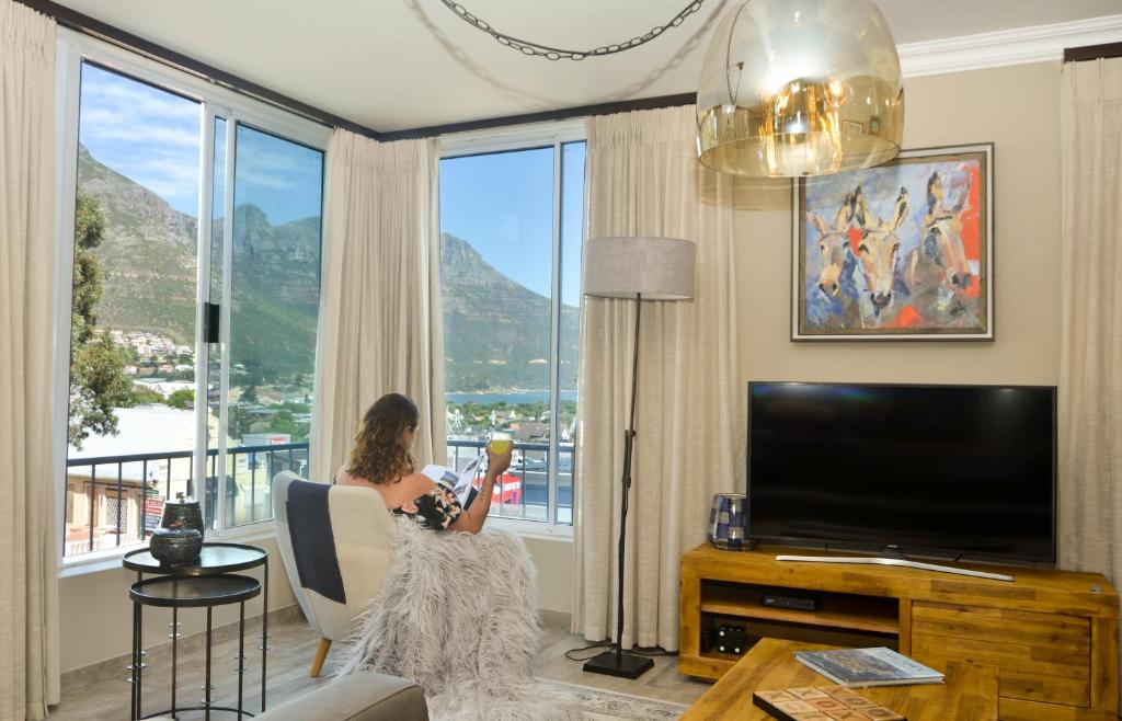 eine Frau auf einem Stuhl in einem Wohnzimmer mit einem großen Fenster in der Unterkunft dk villas 2 The Boardwalk (Hout Bay) in Hout Bay