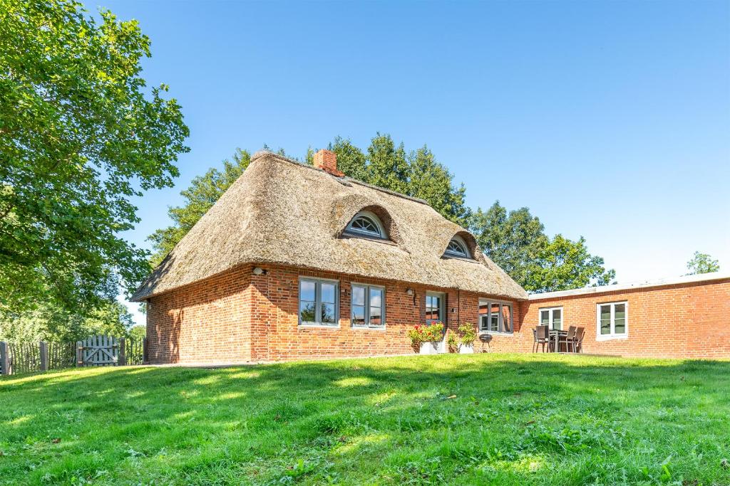 ein Backsteinhaus mit einem Strohdach auf einem Grasfeld in der Unterkunft Kate am See in Uelvesbüll