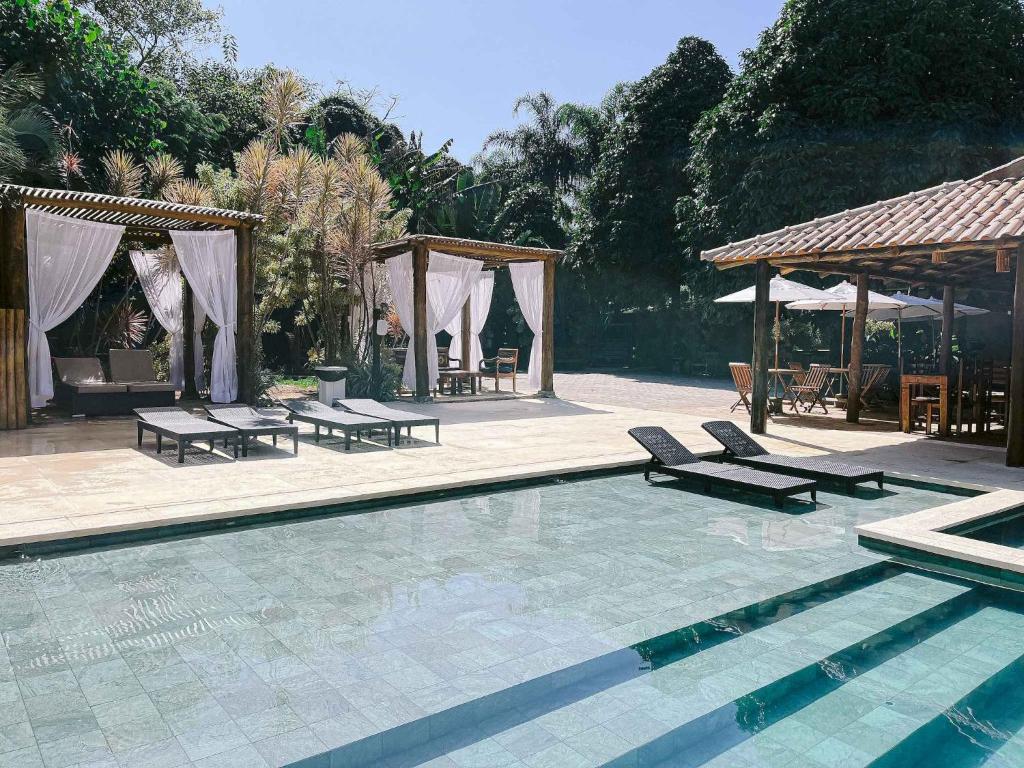 a swimming pool with chairs and a gazebo at Pousada Porto Mare in Maresias