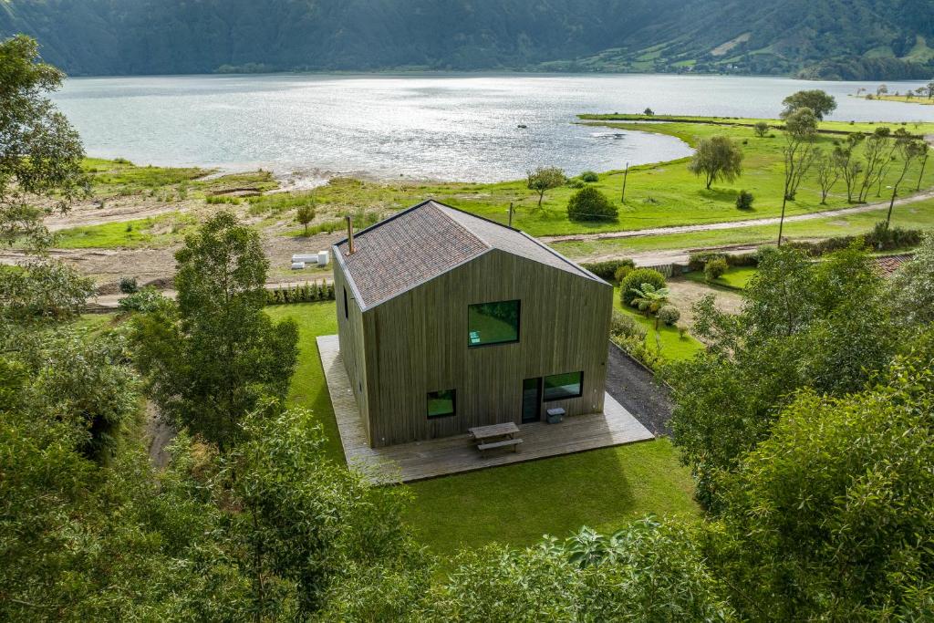 una pequeña casa de madera en un césped junto a un lago en Sete Cidades Lake Cabin - Casa da Lagoa, en Ponta Delgada