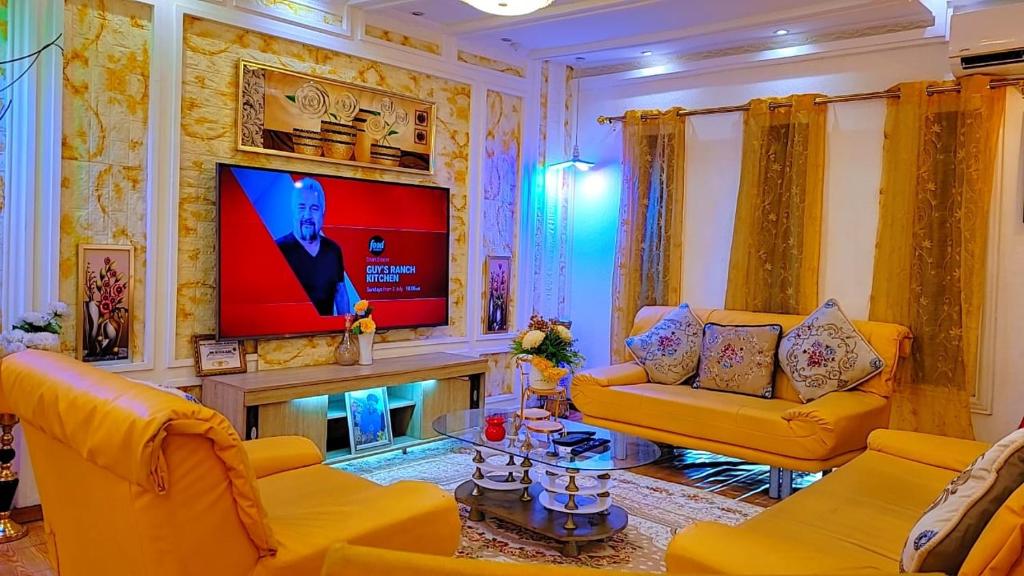 a living room with yellow furniture and a flat screen tv at Golden Aurora Lodge in Kumasi