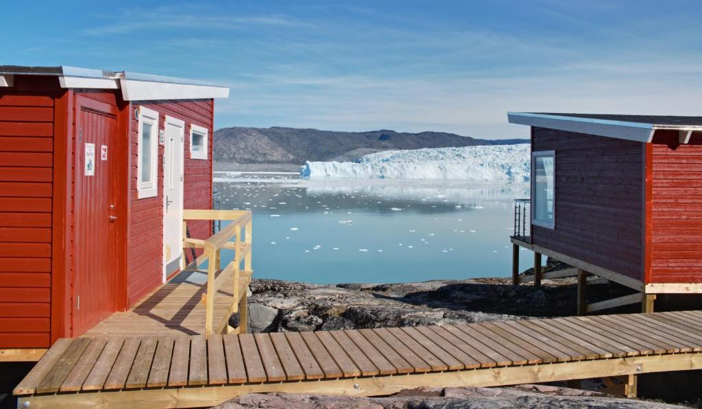 two houses on a dock with a iceberg in the water at Glacier Lodge Eqi in Ilulissat