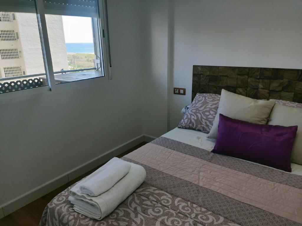 - une chambre avec un lit doté d'oreillers violets et d'une fenêtre dans l'établissement Moderno piso con vista a la playa, à Puebla de Farnals