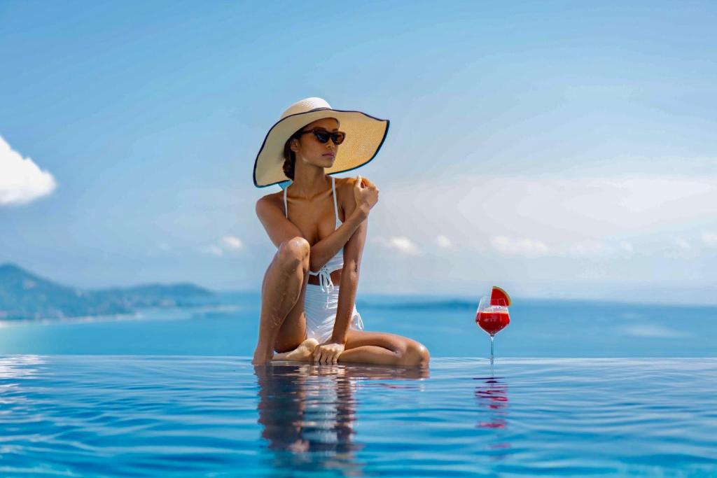 una mujer con sombrero sentada en el agua con una copa de vino en PRIVATE POOL VILLA I Sea Views - Pool - Privacy & Joy, en Chaweng