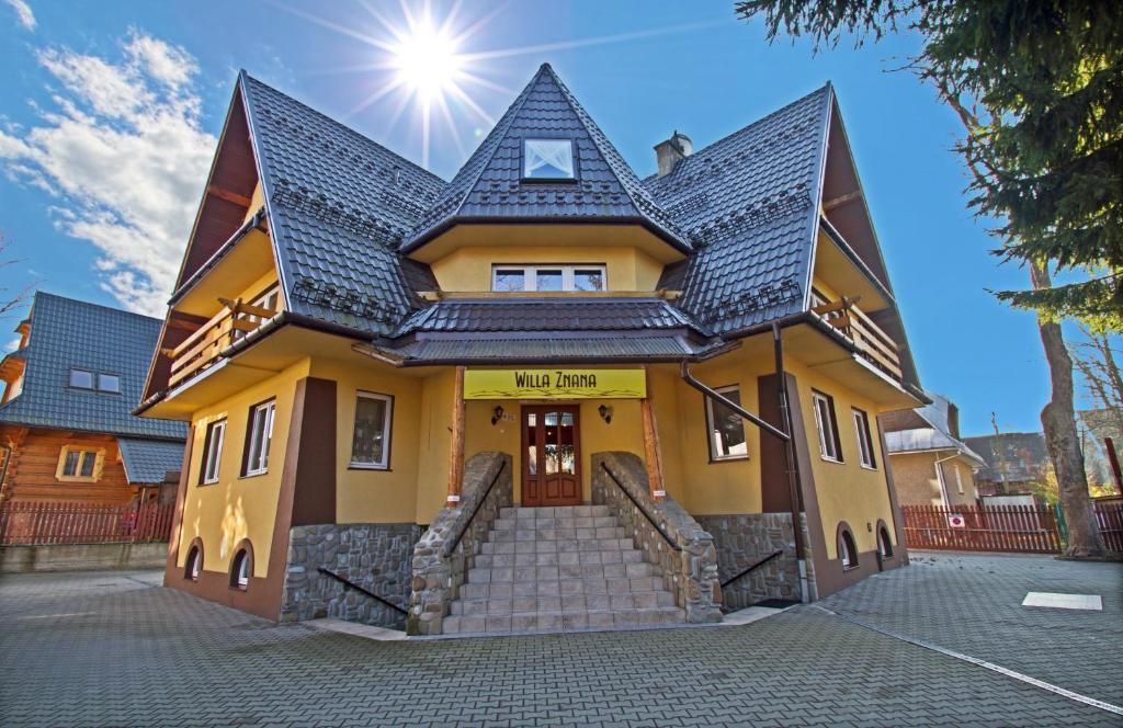 a yellow house with a black roof and stairs at Willa Znana Zakopane in Zakopane
