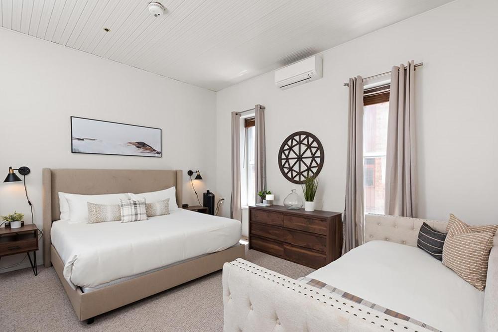 a white bedroom with two beds and a couch at Independence Square 211, Chic Hotel Room with Mountain Views, A/C, & Rooftop Hot Tub in Aspen