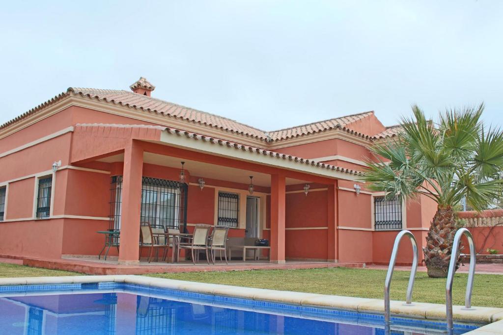 una casa roja con una piscina frente a ella en Chalet Carlos El Campito, en Chiclana de la Frontera