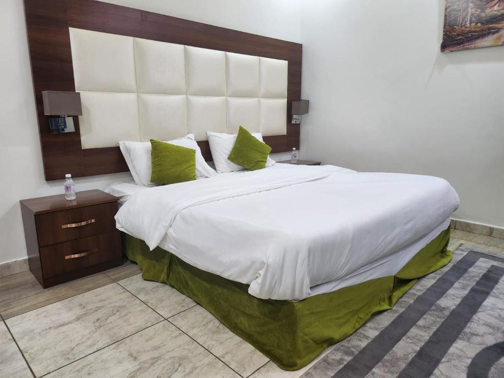 a bedroom with a large white bed with green pillows at طرف الطريق in Al Ḩawīyah