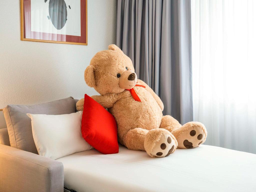 a teddy bear sitting on a bed with a red pillow at Novotel Glasgow Centre in Glasgow