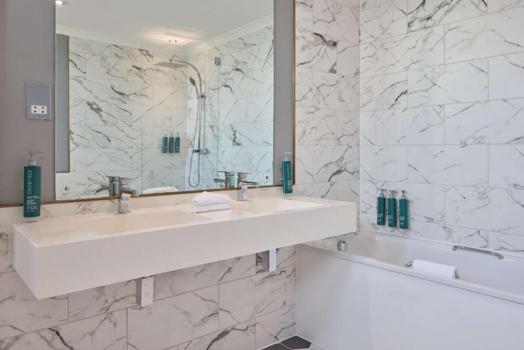 a white bathroom with a sink and a tub at DoubleTree By Hilton Brighton Metropole in Brighton & Hove