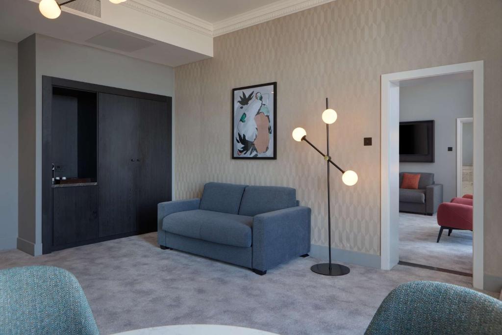 a living room with a blue chair and a lamp at DoubleTree By Hilton Brighton Metropole in Brighton & Hove