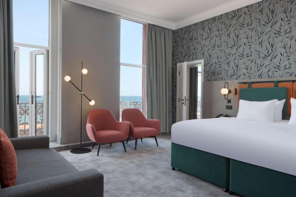 a hotel room with a bed and chairs and windows at DoubleTree By Hilton Brighton Metropole in Brighton & Hove