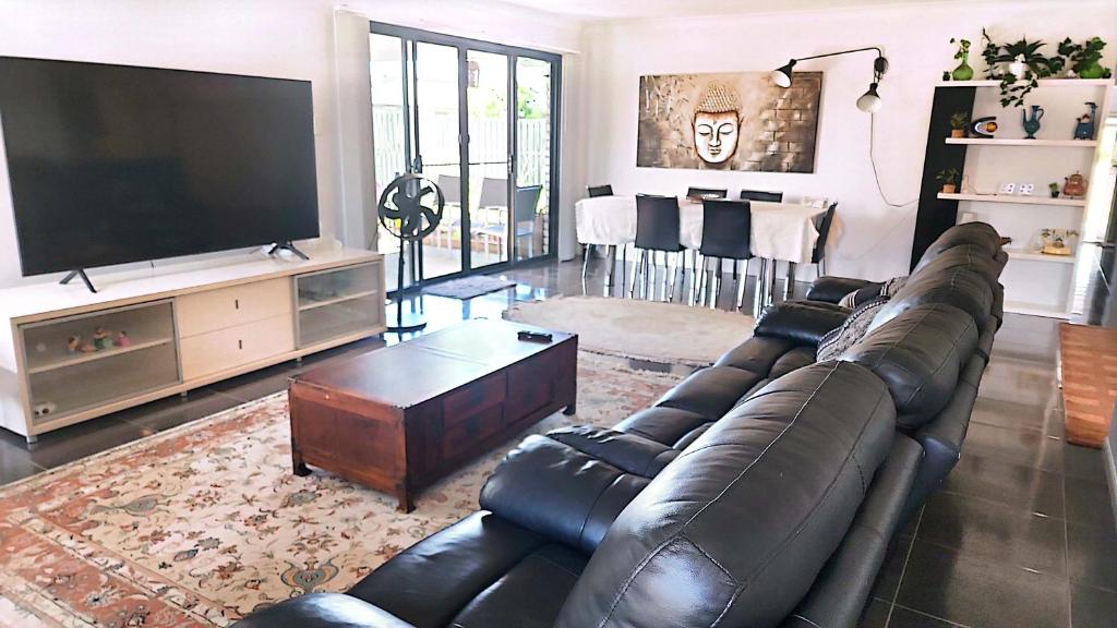 uma sala de estar com um sofá de couro e uma televisão de ecrã plano em Kumera Home em Gold Coast