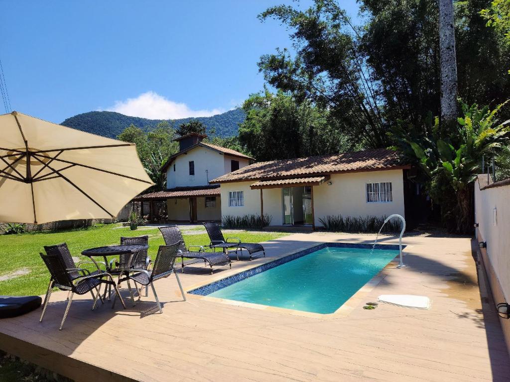 a pool with chairs and a table and an umbrella at Maresias Suítes in Maresias