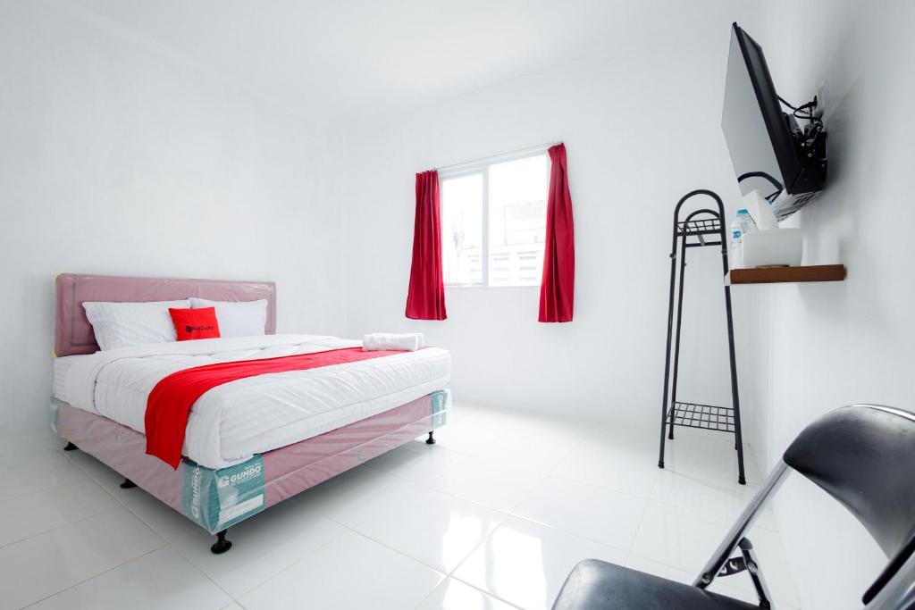 a white bedroom with a bed and a chair at RedDoorz near Jalan Cikini in Jakarta