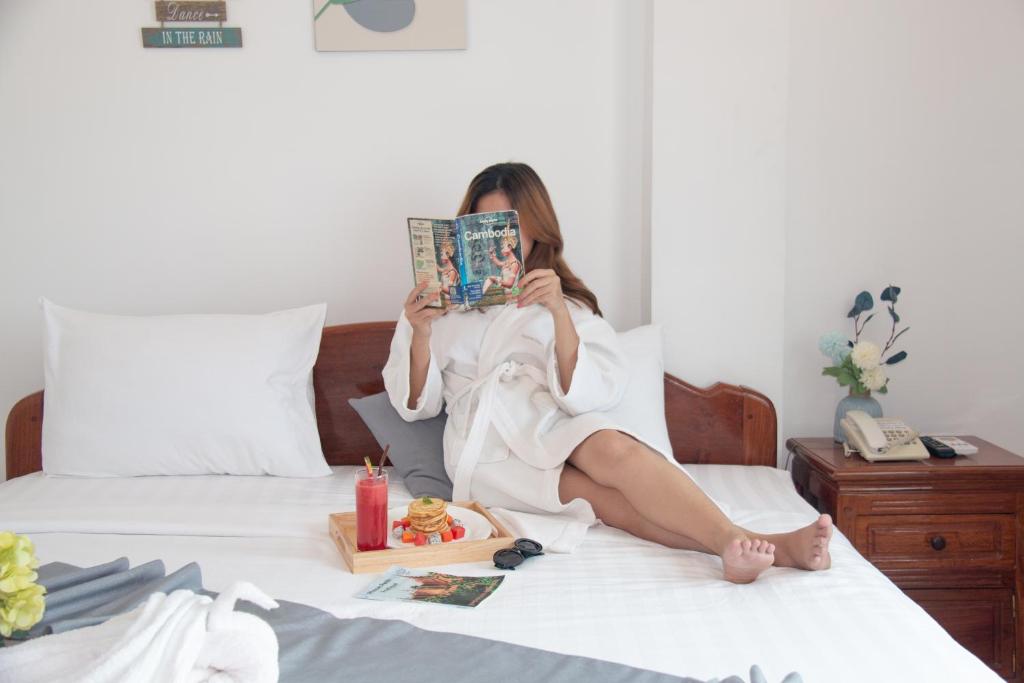 Una donna seduta su un letto che legge una rivista di White Corner Hotel a Phnom Penh