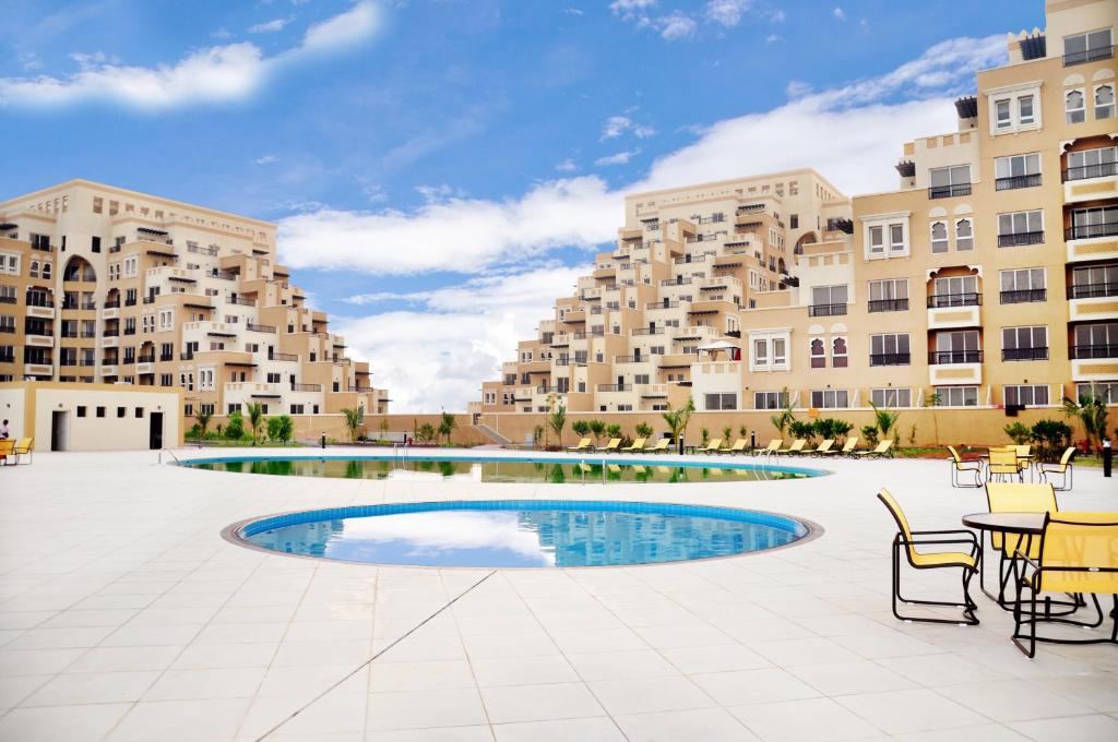 a large apartment complex with a pool and tables and chairs at Clarence Apartment in Ras al Khaimah