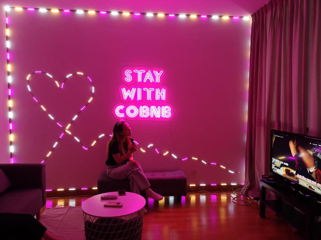 a woman sitting in a living room with a neon sign at KL Gateway Penthouse w Karaoke by Cobnb in Kuala Lumpur