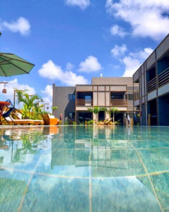 a large swimming pool with a building and an umbrella at Mani Milagres Studio - Gamboa Patacho in Pôrto de Pedras