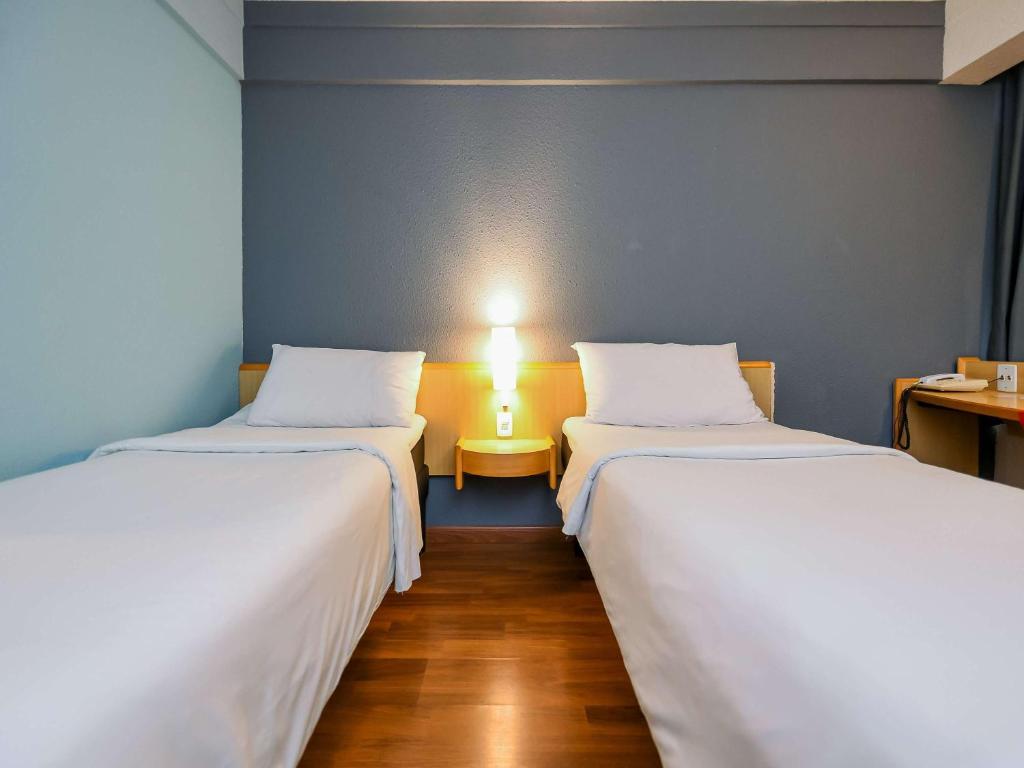 two beds in a room with a lamp between them at ibis Guarulhos Aeroporto in Guarulhos