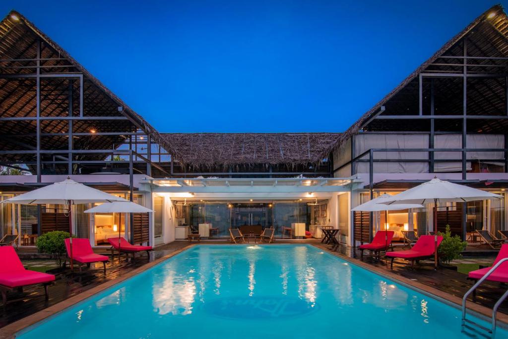 una piscina con sillas y sombrillas rojas en StayVista at The Rain - River Villa with Infinity Pool, en Alleppey