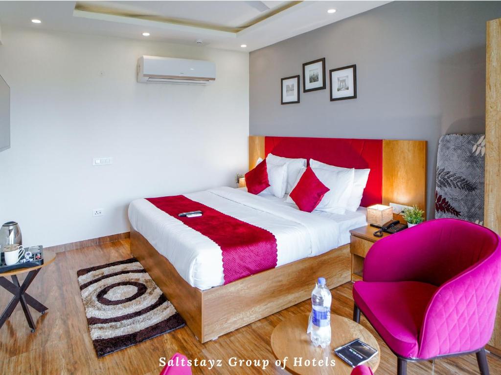 a bedroom with a large bed and a pink chair at Saltstayz Hotel Huda City Centre in Gurgaon