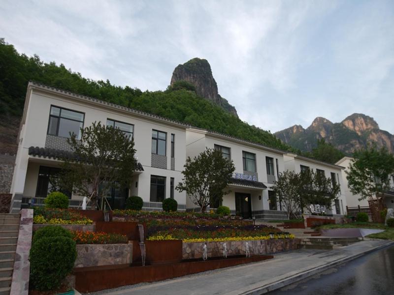 a large white building with mountains in the background at Feronia Hotel Taihang Xiyagou Tourist Area in Nanhekou