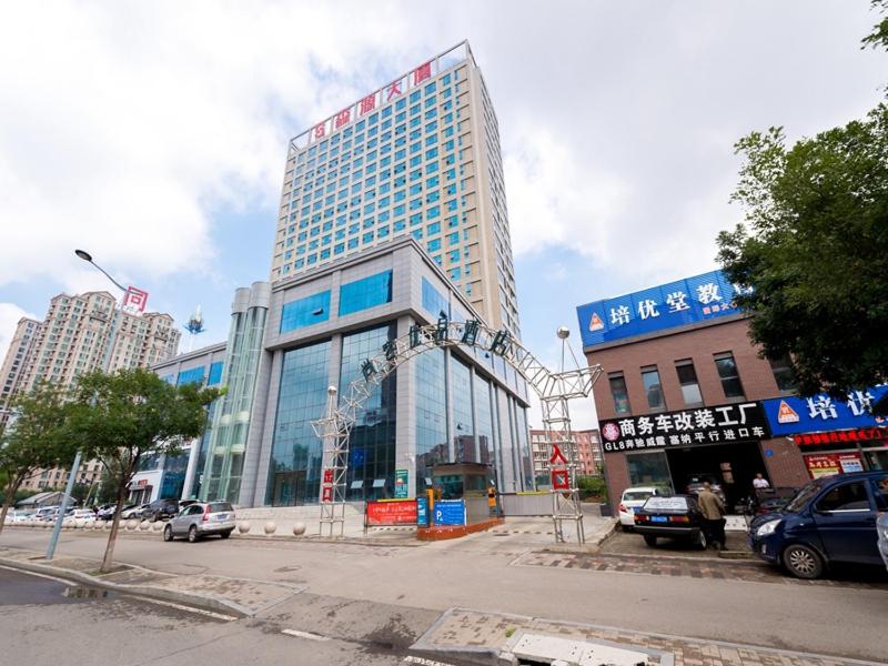 un gran edificio de cristal en una calle de la ciudad con coches en Thank Inn Plus Datong Senyuan Building High-Speed Railway Station, en Datong