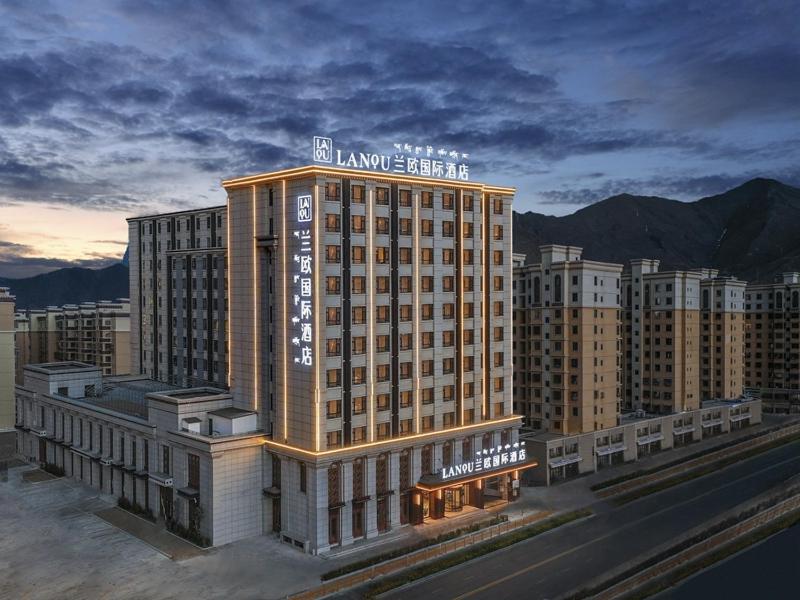 LanOu Hotel Lhasa Municipal Government Tibet University في لاسا: تقديم عمارة فندقية بالجبال في الخلفية